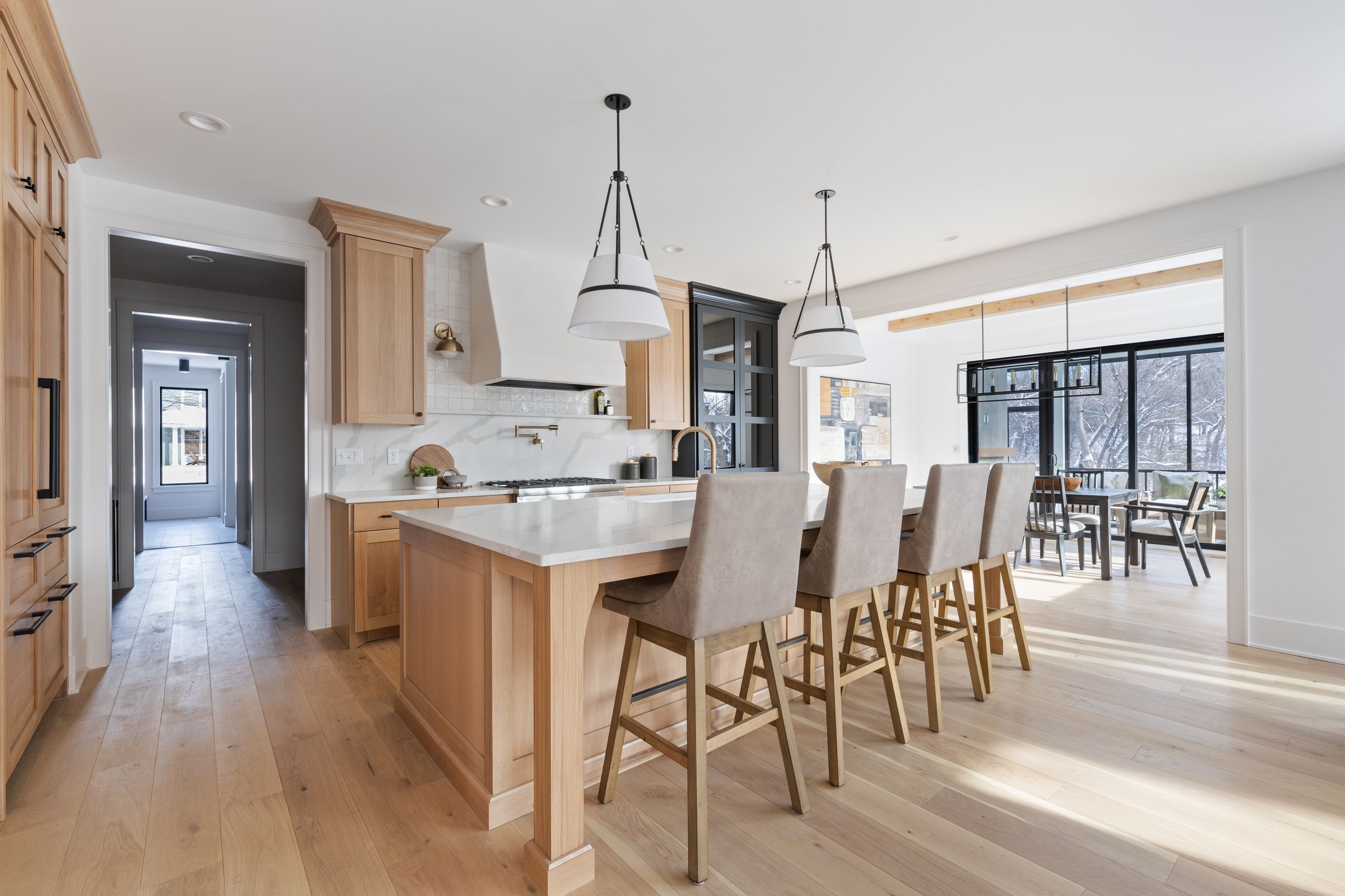 Kitchen with white oak cabinetry, a plaster range hood, a long island with four stools, and a dining area beyond