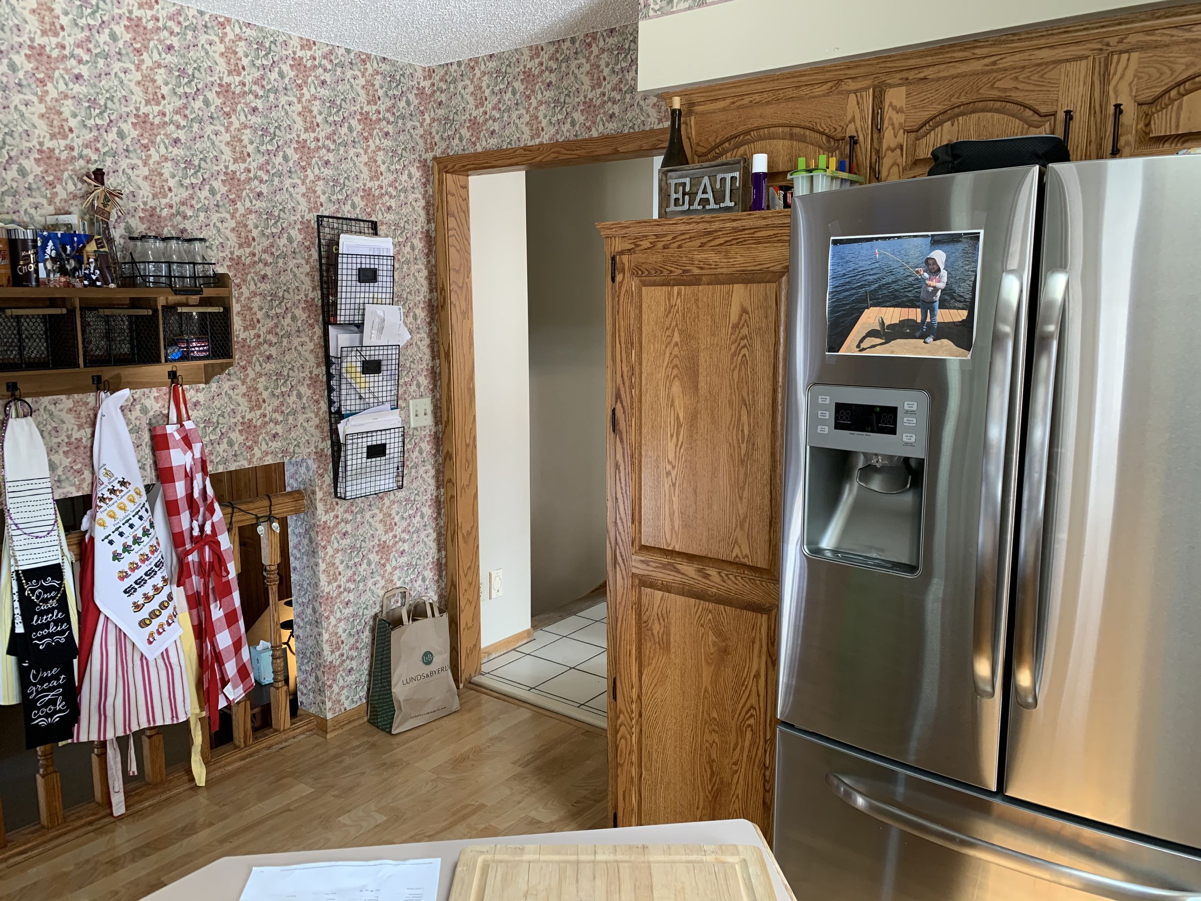 Before, the kitchen had oak cabinets, floral wallpaper, and a closed-off doorway to the back hall