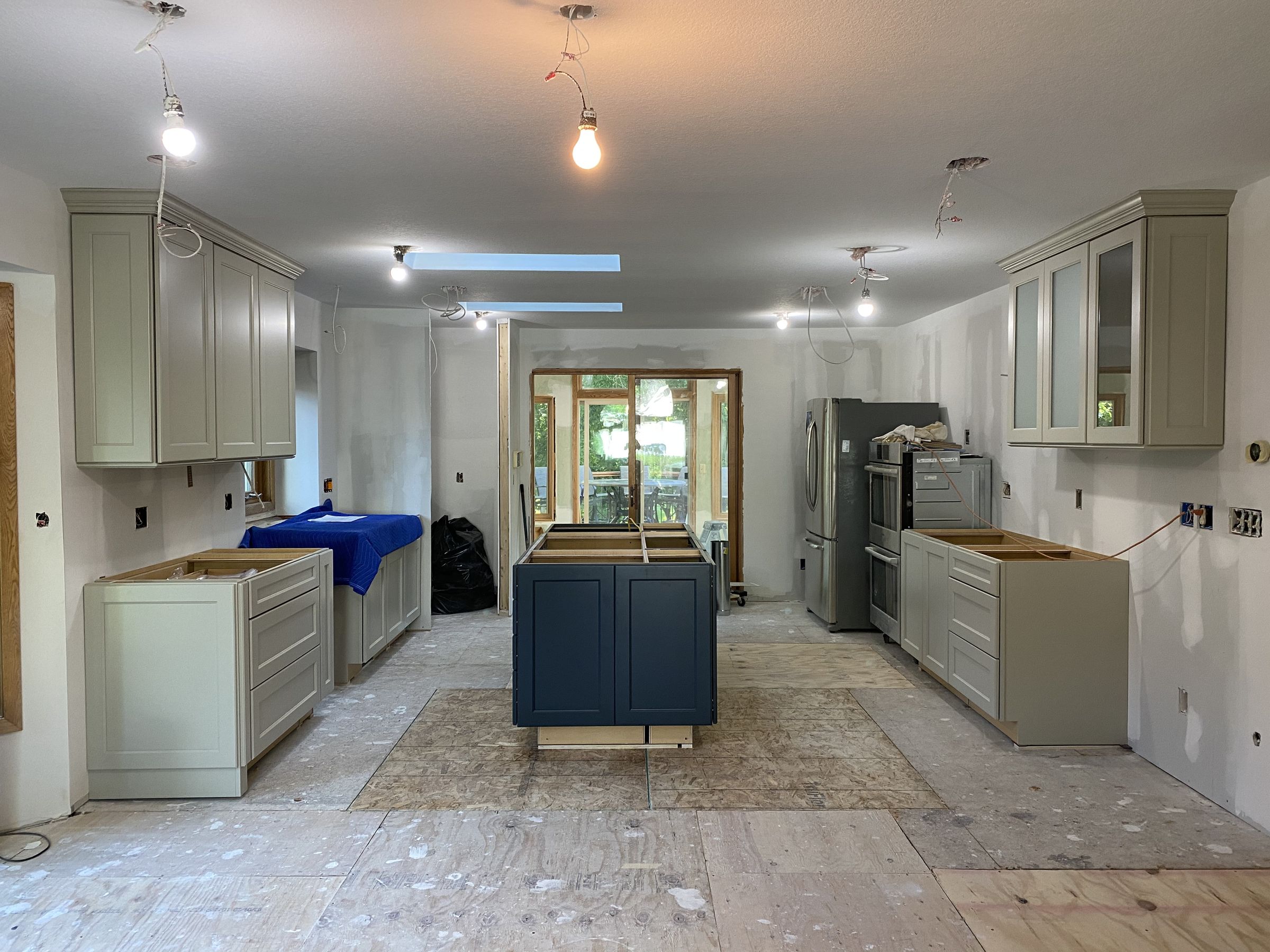 New gray cabinets and a navy island being installed, with the light locations wired in the ceiling