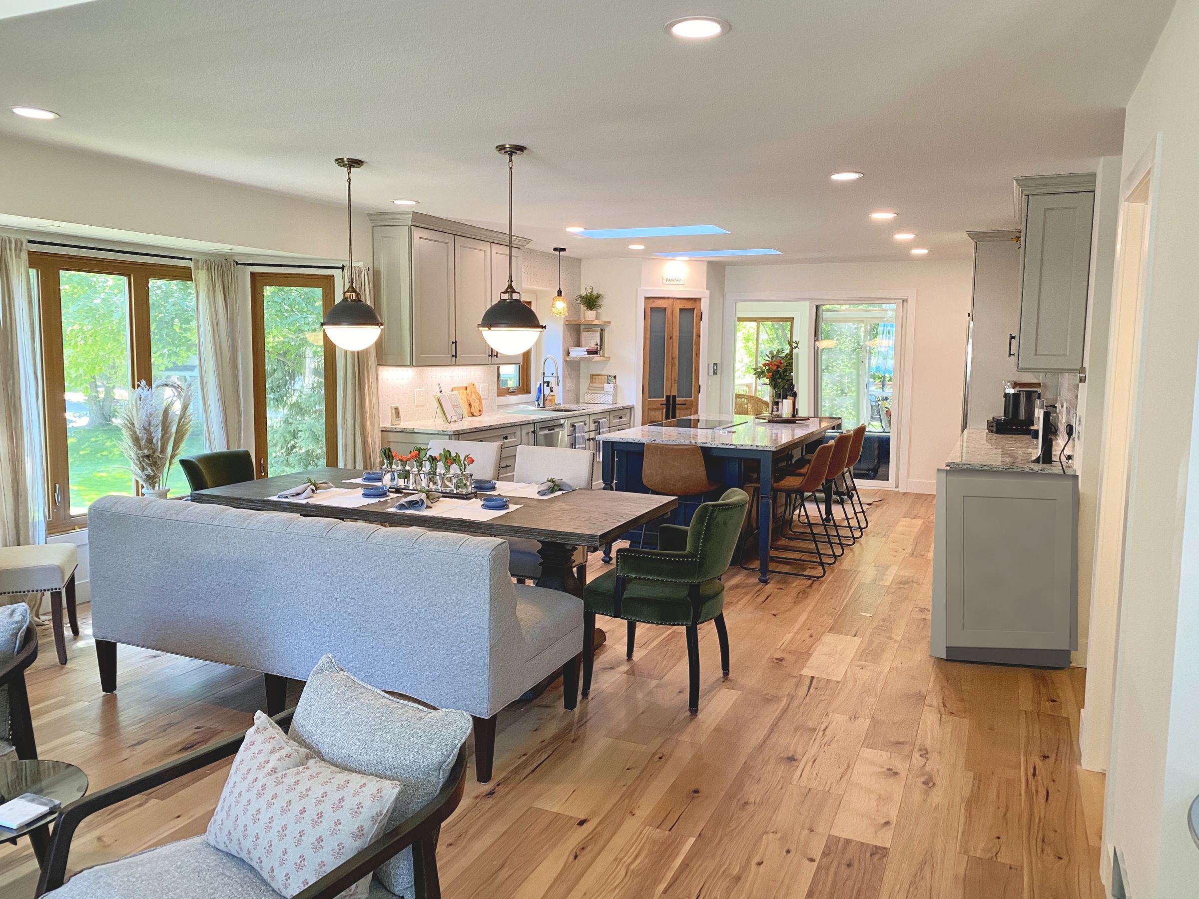 The opened-up main level, with a long navy island, gray cabinetry, globe pendants over a plank-top dining table, and a wall of windows