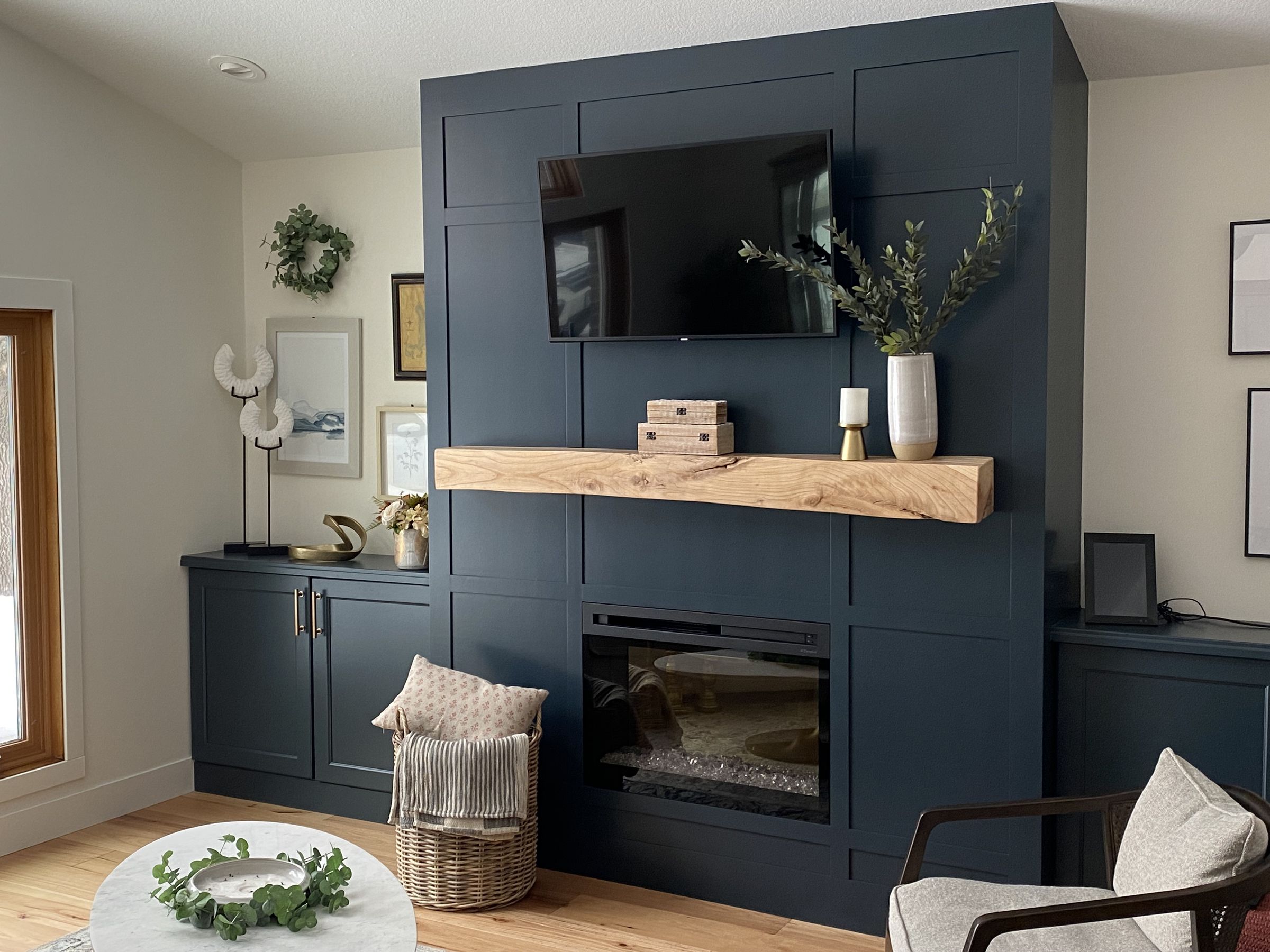 Navy paneled fireplace wall with a wood beam mantel, a mounted TV, and matching built-in cabinets on either side