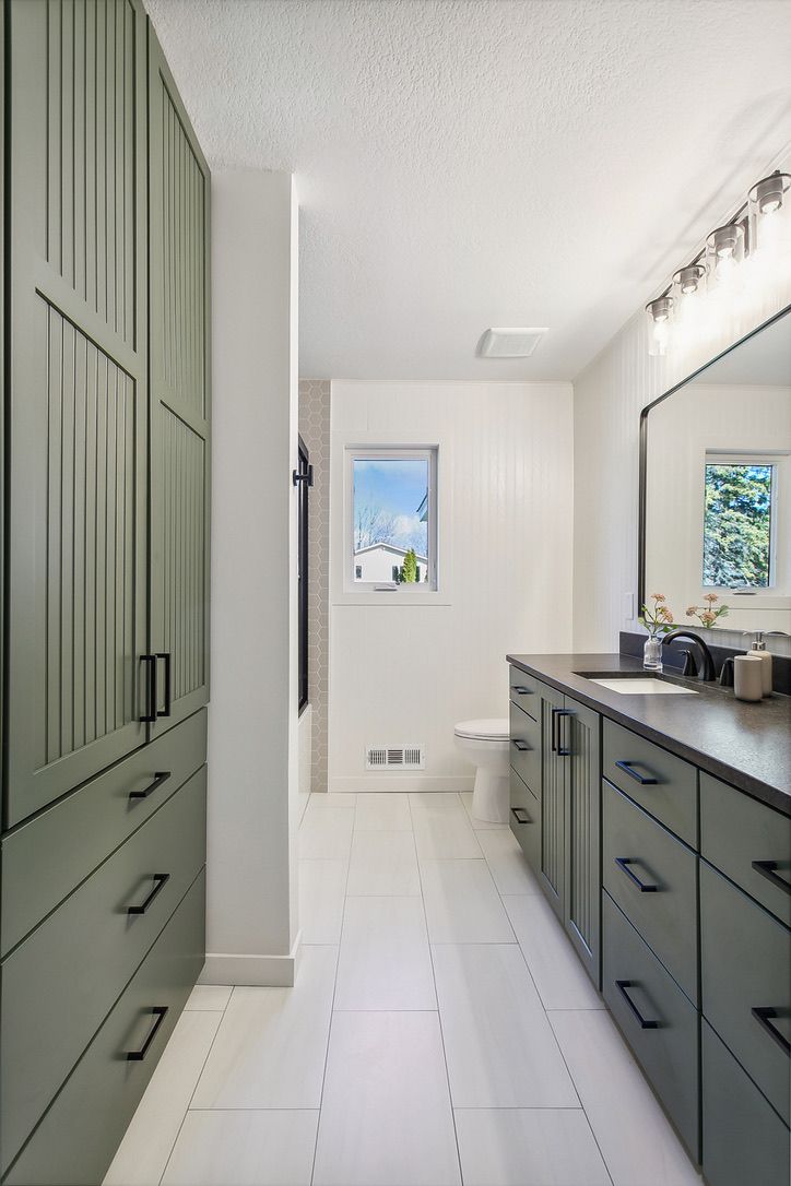 Bathroom with green beadboard linen cabinets and a matching vanity with black pulls, white beadboard walls, and a large format tile floor