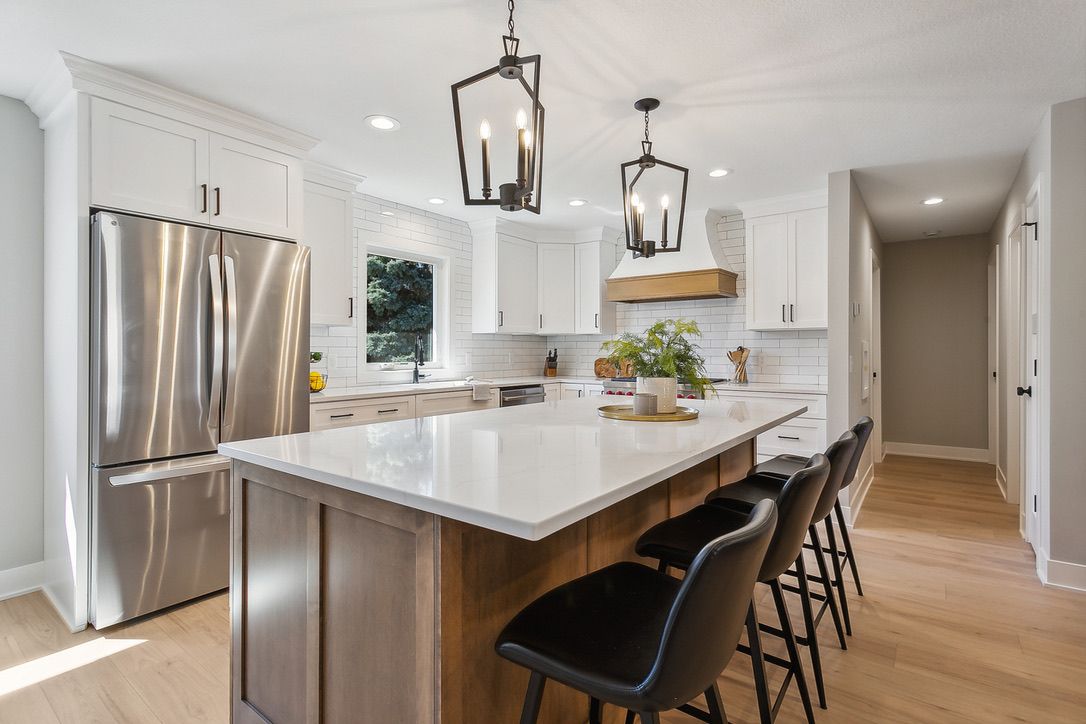 Renovated kitchen with white shaker cabinetry, a stained wood island, and black lantern pendants