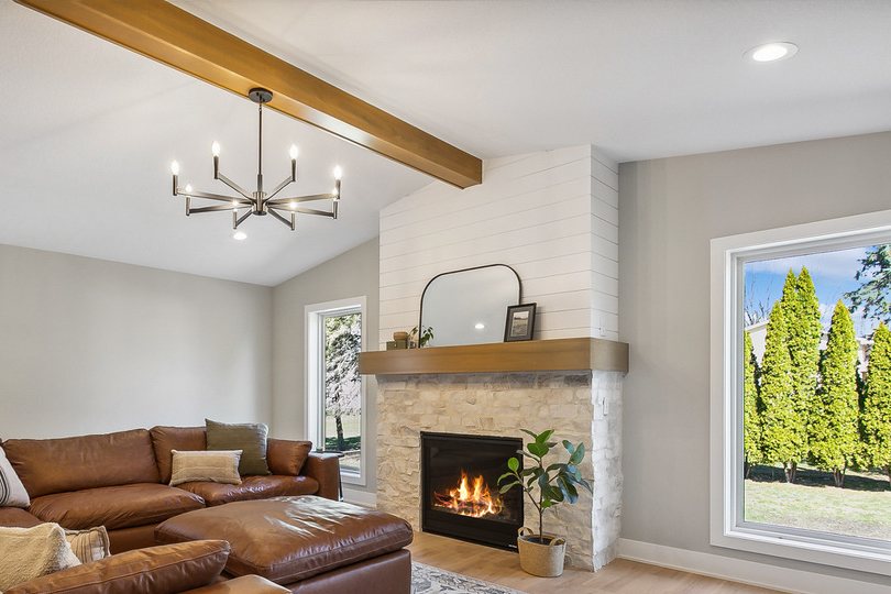 Living room fireplace with a shiplap surround, stacked stone base, and wood mantel under a vaulted ceiling with a stained beam and a black candle chandelier