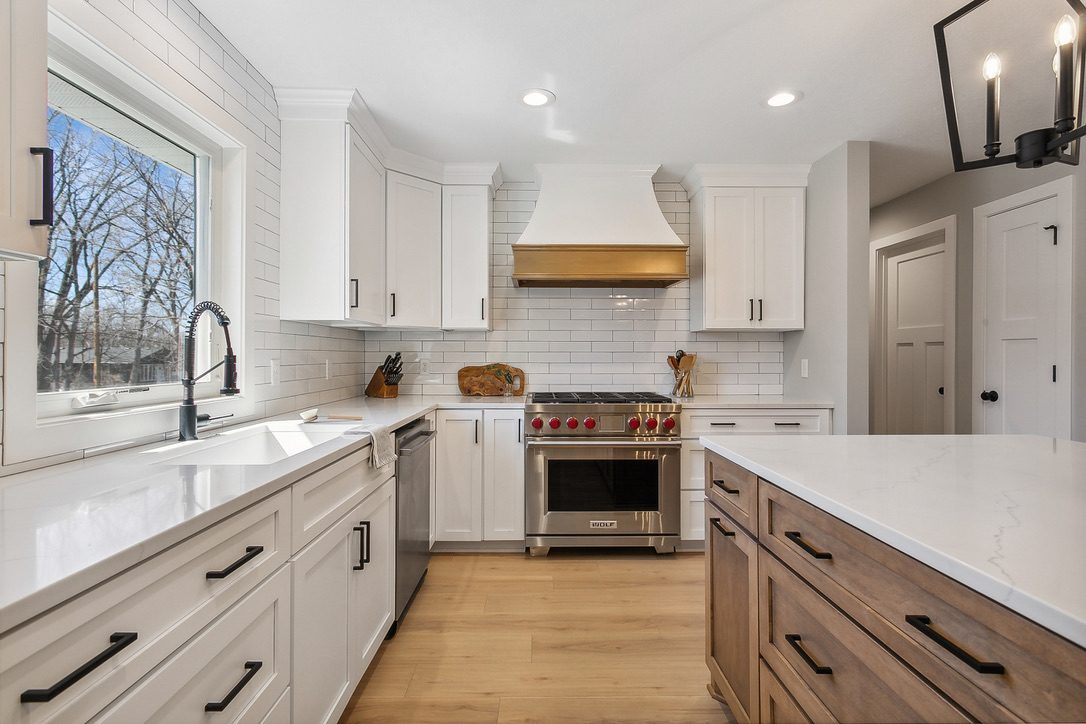 Kitchen with white shaker cabinetry to the ceiling, a white range hood with a brass band over a pro range, white subway tile, and a stained wood island with a white quartz top